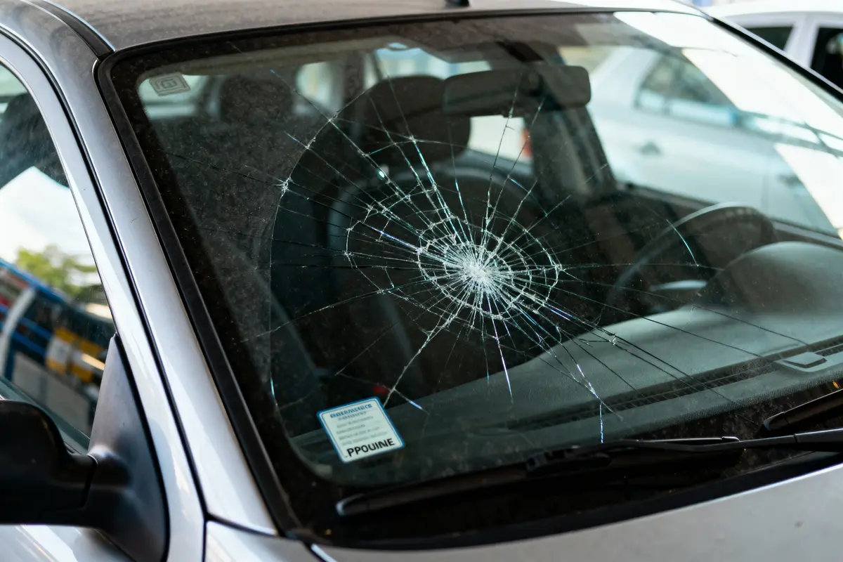 Pare-brise de voiture avec impact central étoilé et fissures rayonnantes sur surface.루