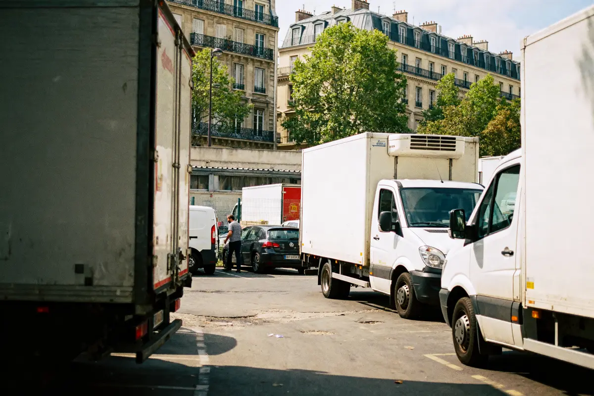 Camions blancs garés près d'un immeuble parisien, un homme se tient à côté d’un utilitaire.