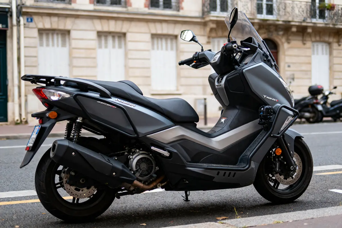 Scooter noir stationné dans une rue bordée de bâtiments en pierre avec fenêtres fermées.