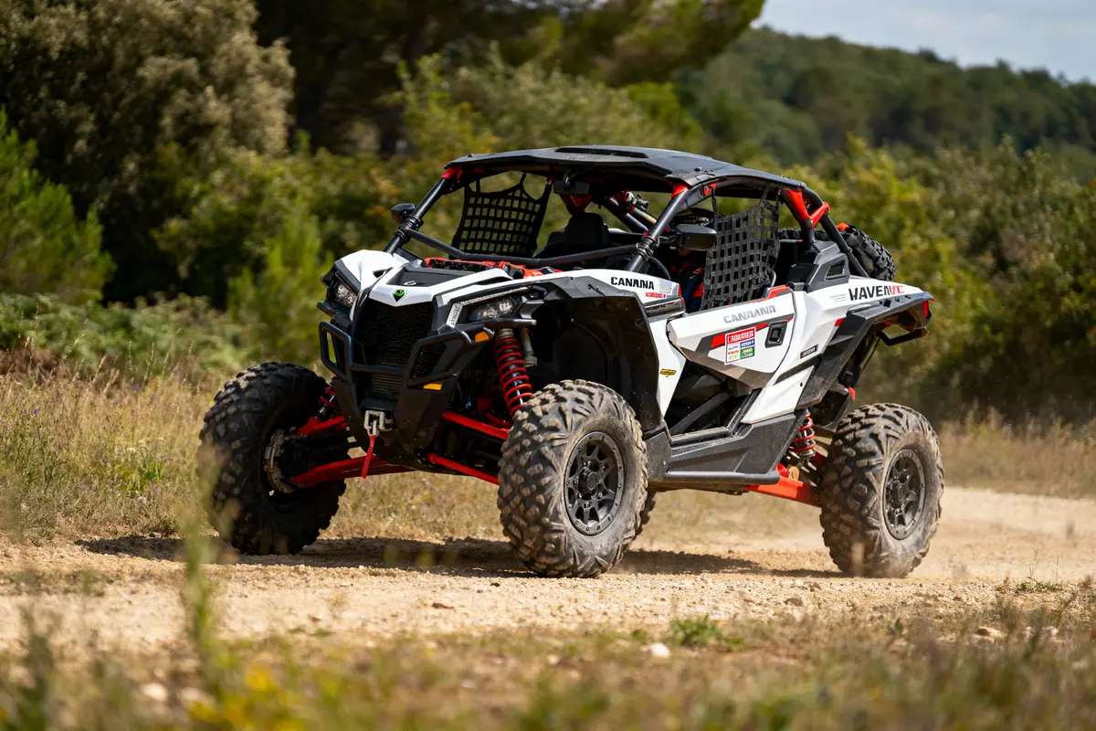 Buggy tout-terrain blanc et rouge traversant un chemin de terre, entouré de végétation et d'arbres, en pleine action.