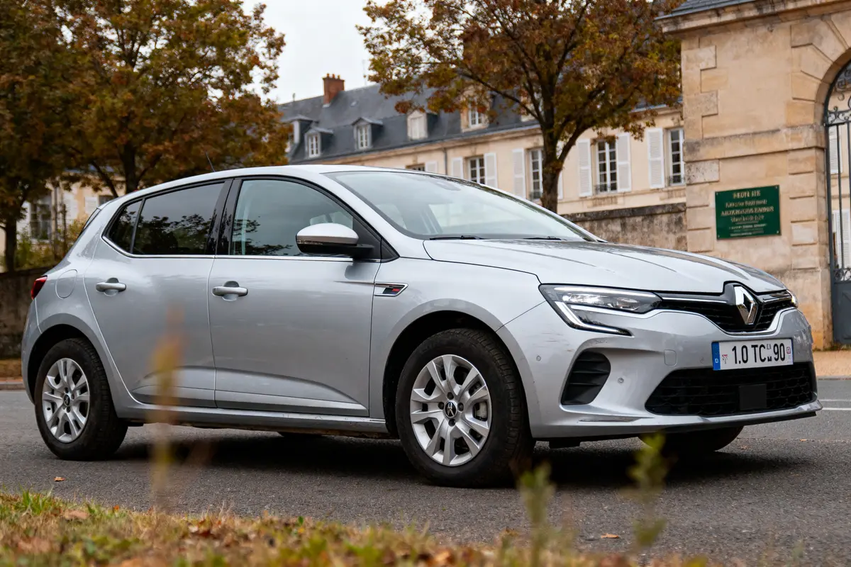 Voiture Renault grise garée devant bâtiment historique, arbres en arrière-plan, plaque d'immatriculation visible.