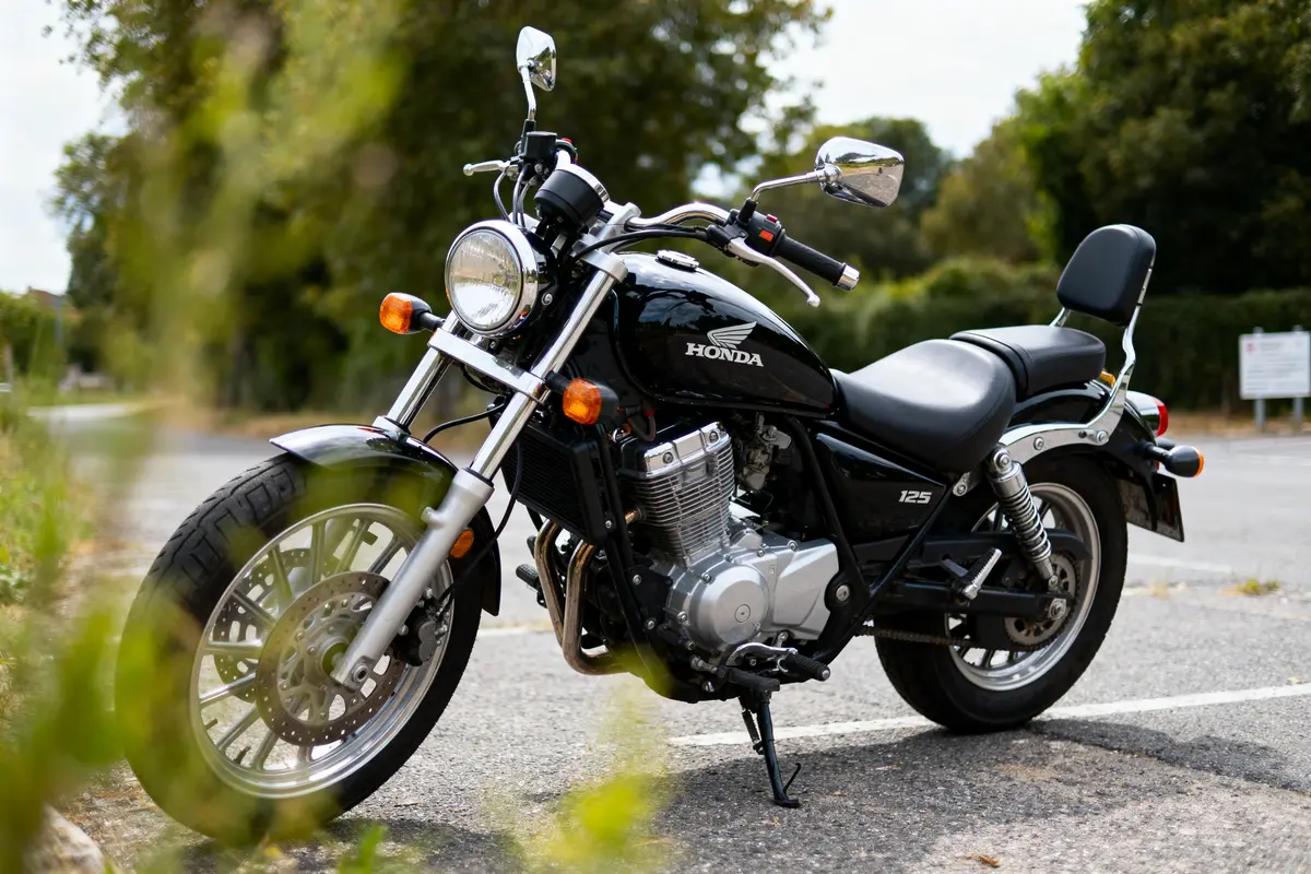 Moto Honda noire garée sur la route, entourée de végétation, vue de côté avec ciel nuageux.