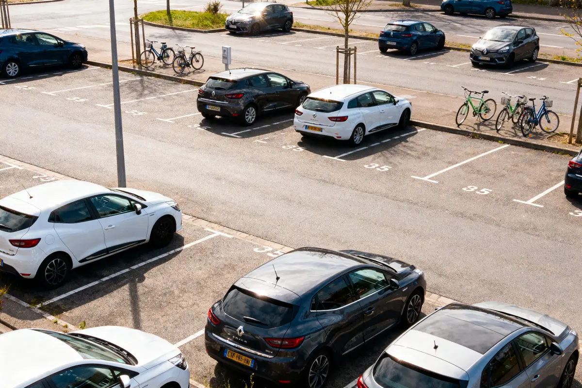 Vue aérienne d'un parking avec voitures garées et vélos stationnés sur le trottoir.