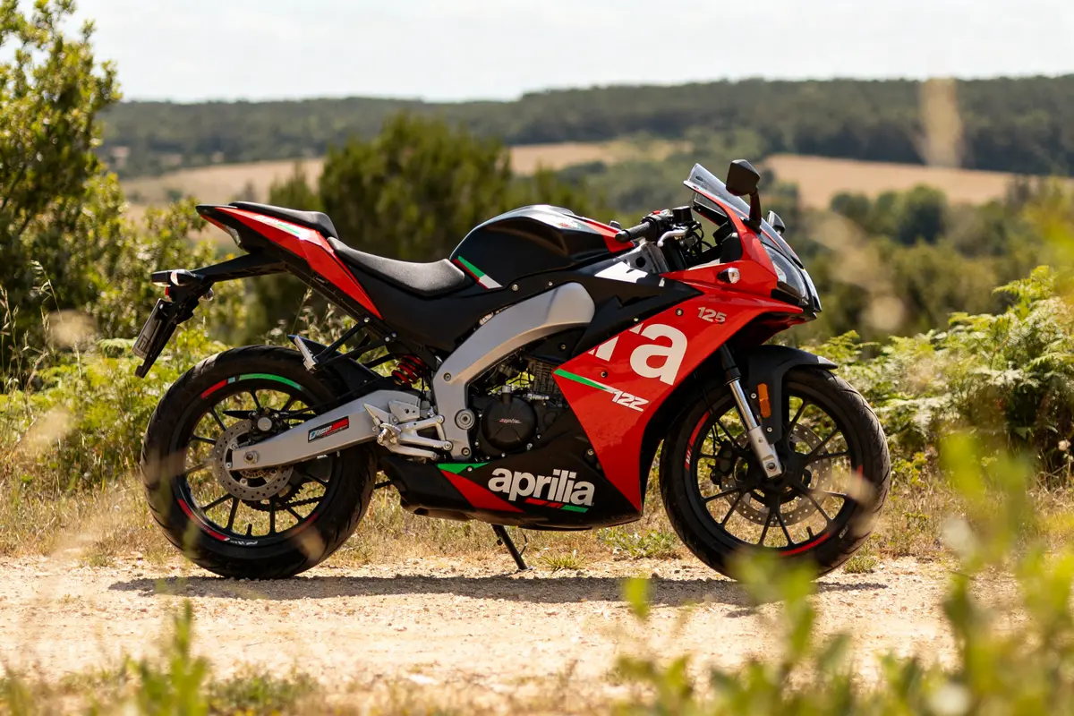 Moto sportive Aprilia RS 125 rouge et noire sur chemin rural ensoleillé