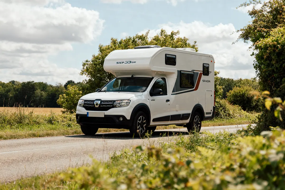 Camping-car Dacia StepCamper roulant sur route de campagne en été avec ciel nuageux