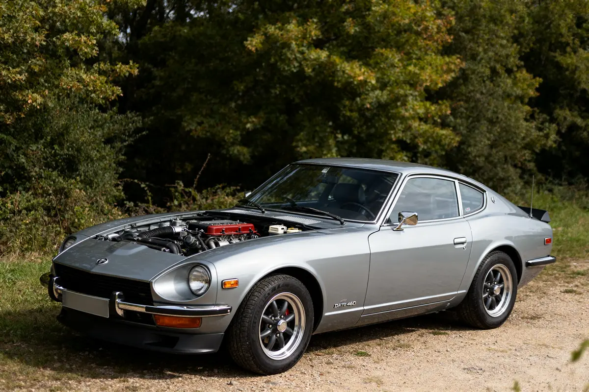 Voiture classique Datsun 240z automatic argent avec capot ouvert sur chemin forestier