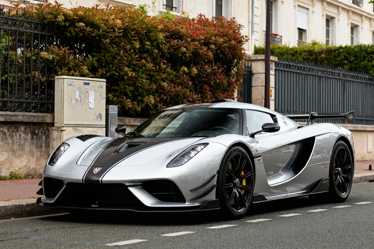 Voiture de sport grise sur route urbaine devant villa verte Hennessey Venom F5