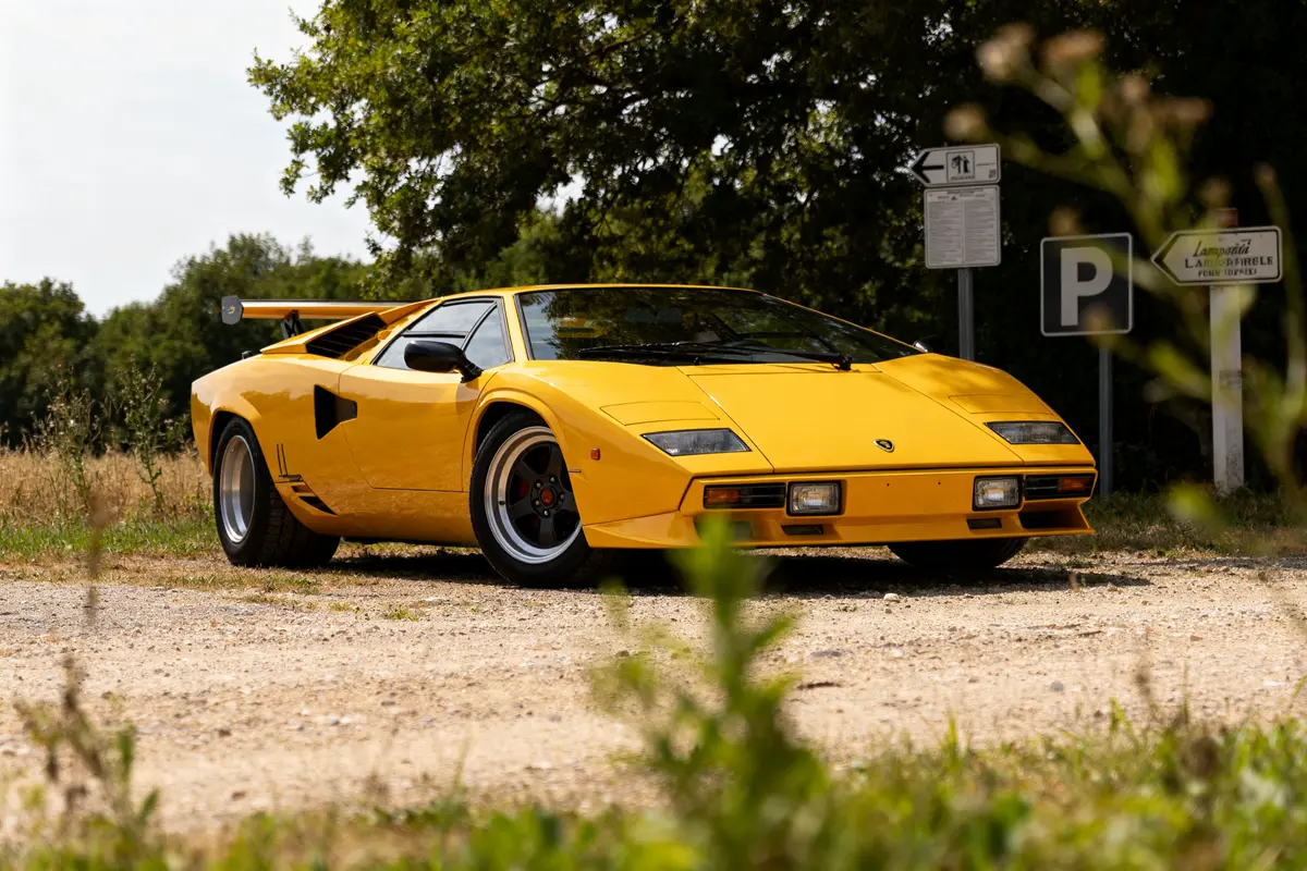 Lamborghini Countach jaune stationnée en extérieur, entourée de végétation et panneaux routiers.