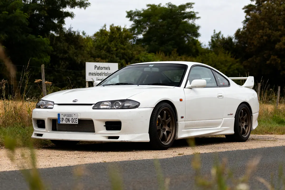 Nissan Silvia S15 blanche garée sur une route de campagne entourée d'arbres verdoyants