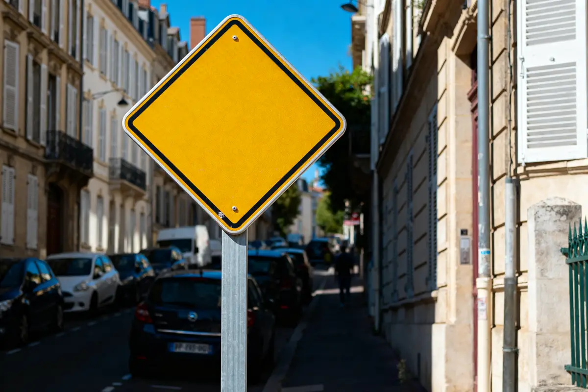 Panneau losange jaune sur fond de rue urbaine avec immeubles et voitures