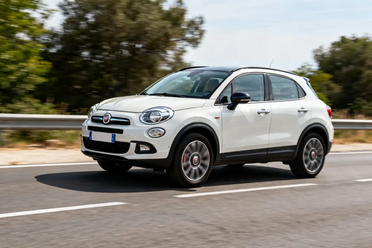 Voiture Fiat 500x blanche roulant sur une route bordée d'arbres en pleine journée