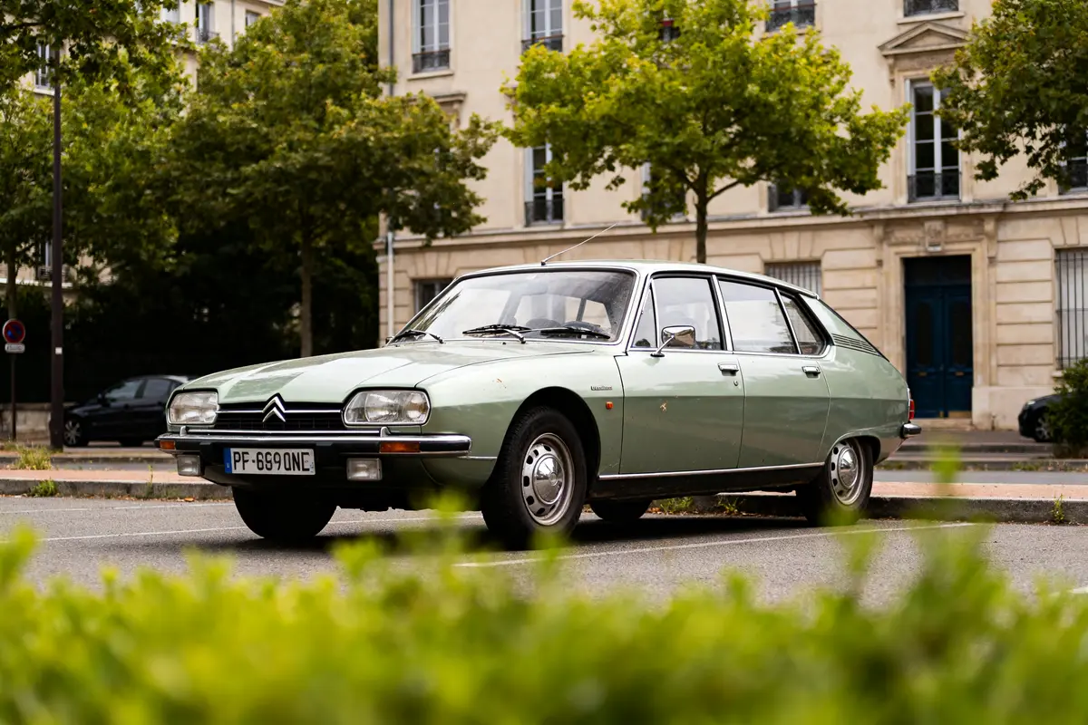 Citroën GS classique vert stationnée devant un bâtiment avec des arbres en arrière-plan