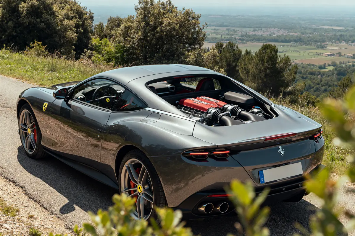 Ferrari Roma grise stationnée, moteur visible, sur route de campagne panoramique