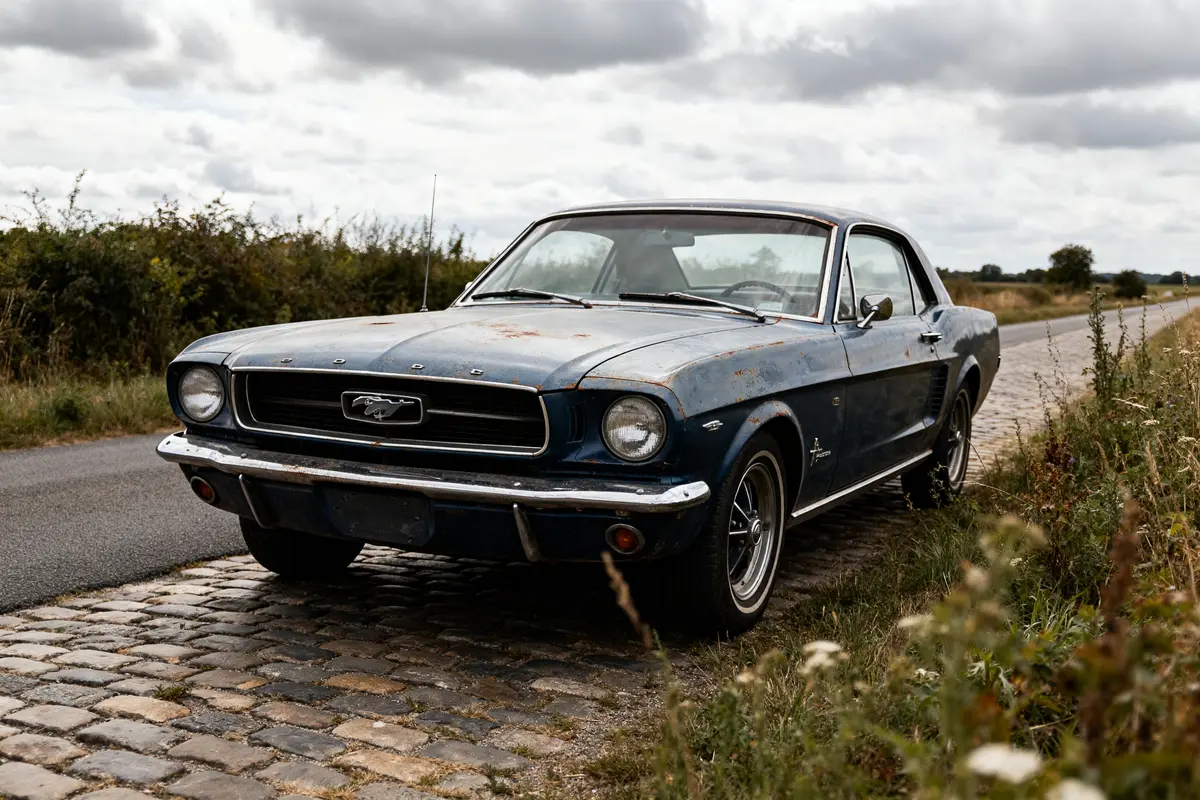 Ford Mustang 1967 bleue garée sur une route pavée en pleine campagne verdoyante