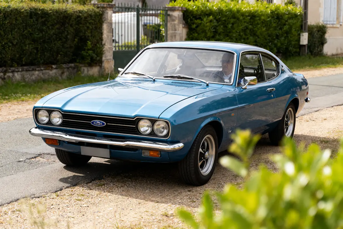 Voiture classique bleue Ford Capri 1970 garée sur une route rurale.