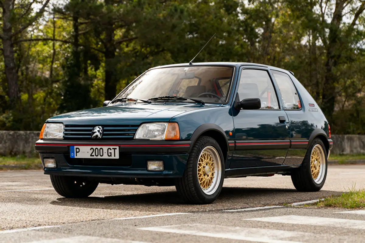 Peugeot 205 GTI automatic bleu avec jantes dorées garée sur une route ensoleillée