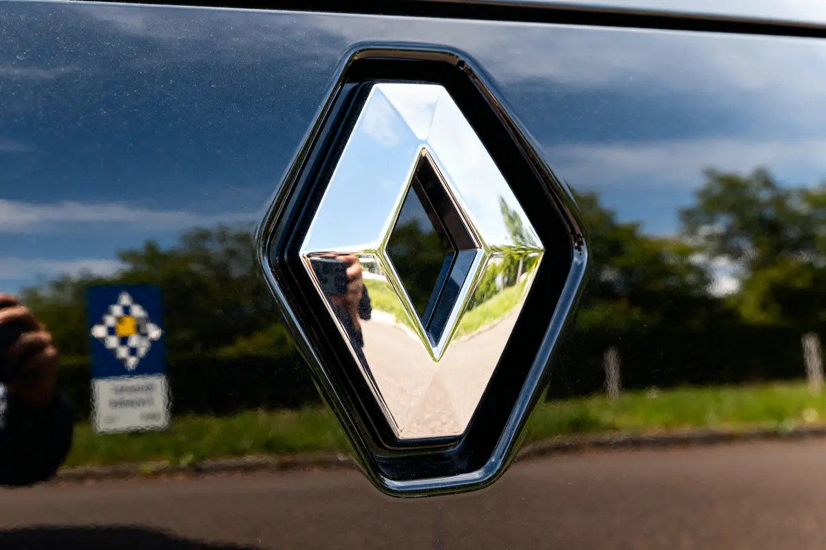 Chrome Renault logo sur carrosserie noire, reflet d'extérieur verdoyant par temps ensoleillé