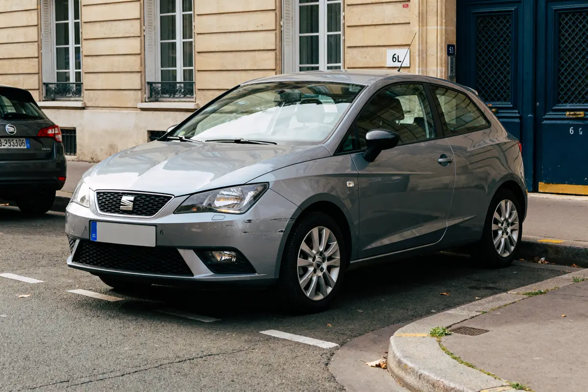 Voiture SEAT ibiza 6L grise garée dans une rue urbaine pavée.
