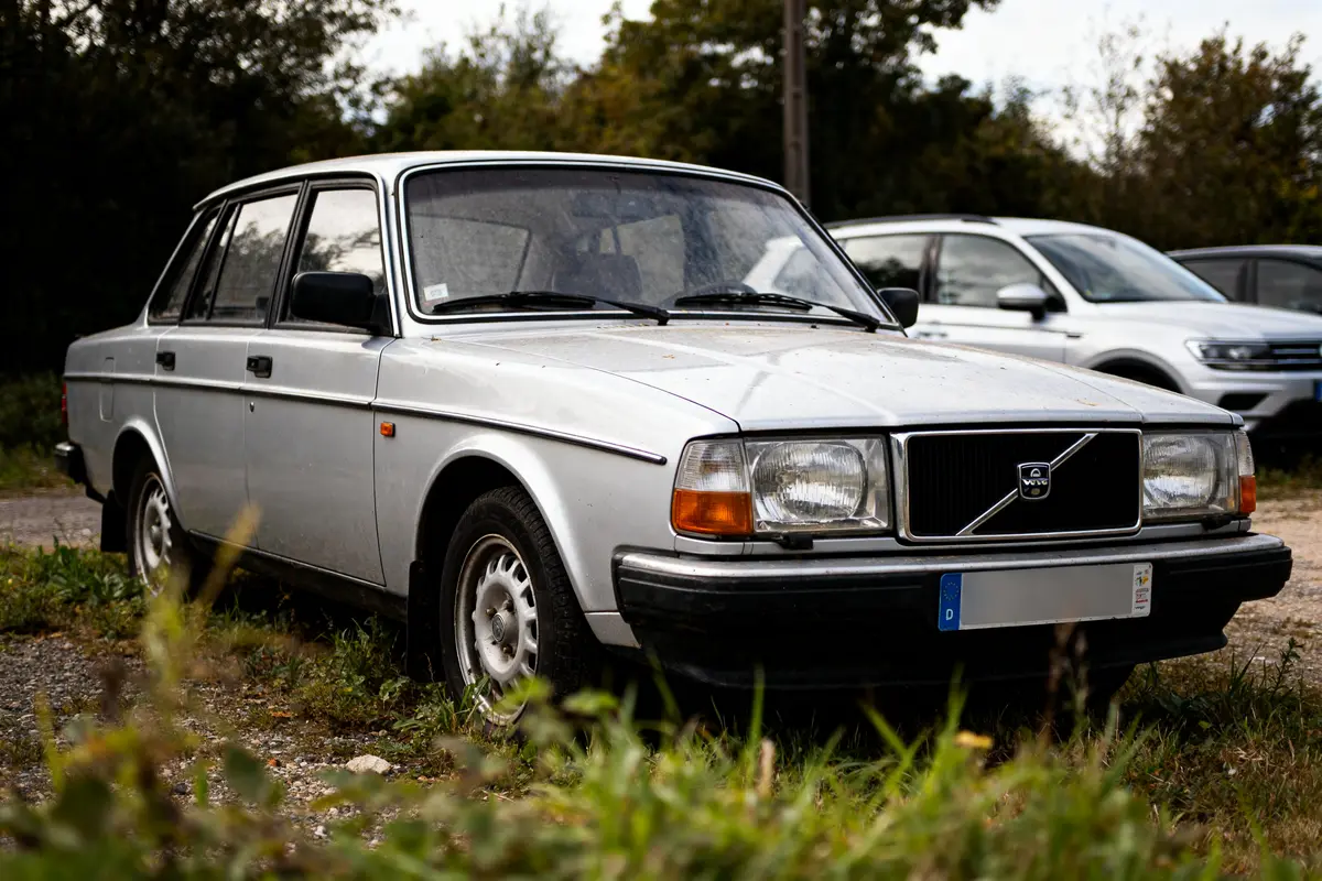 Auto Volvo 240 classique grise garée sur un terrain herbeux avec d'autres voitures derrière