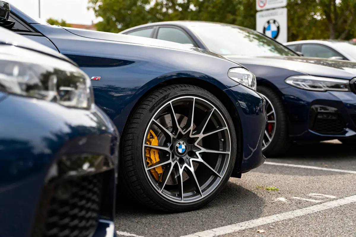 Voiture BMW bleue avec jantes para BMW sur un parking arboré