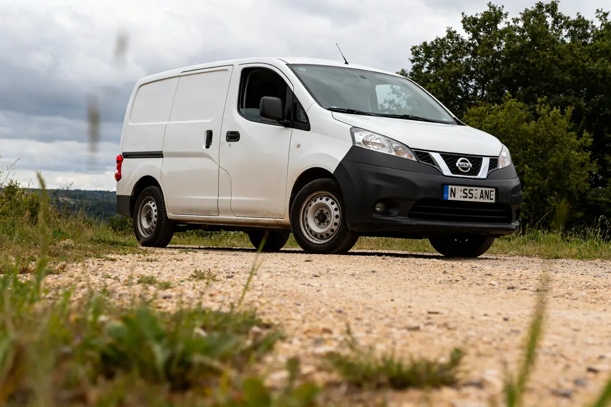 Utilitaire Nissan blanc garé sur un chemin de terre devant des arbres verdoyants