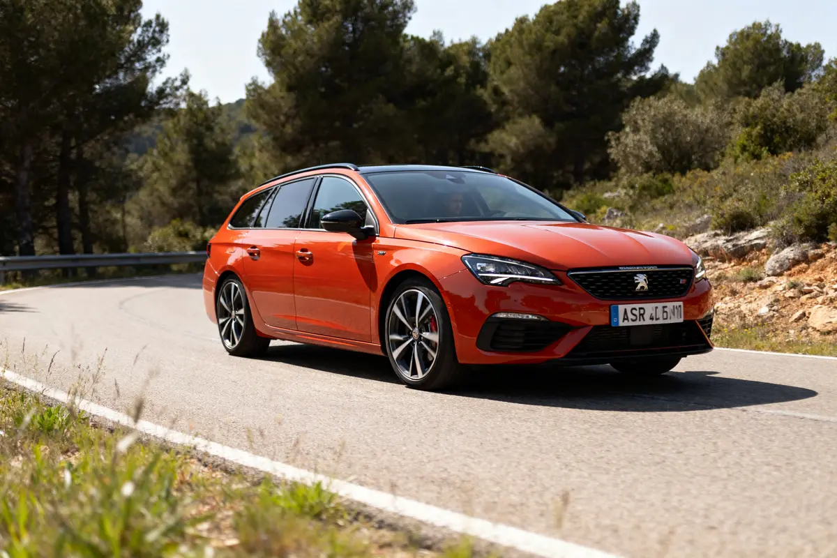 Voiture orange roulant sur route sinueuse sous un ciel dégagé avec plaque ASR.