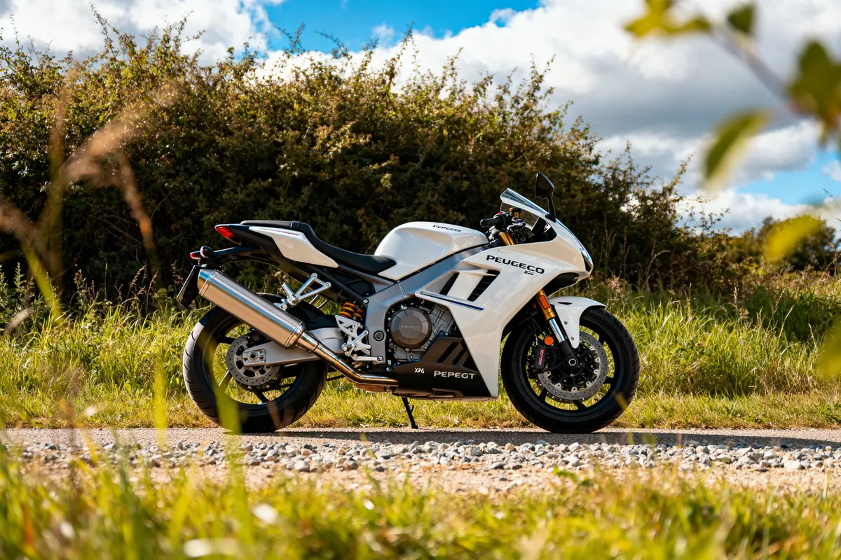 Moto blanche Peugeot XP6 sur chemin de gravier, paysage naturel en arrière-plan