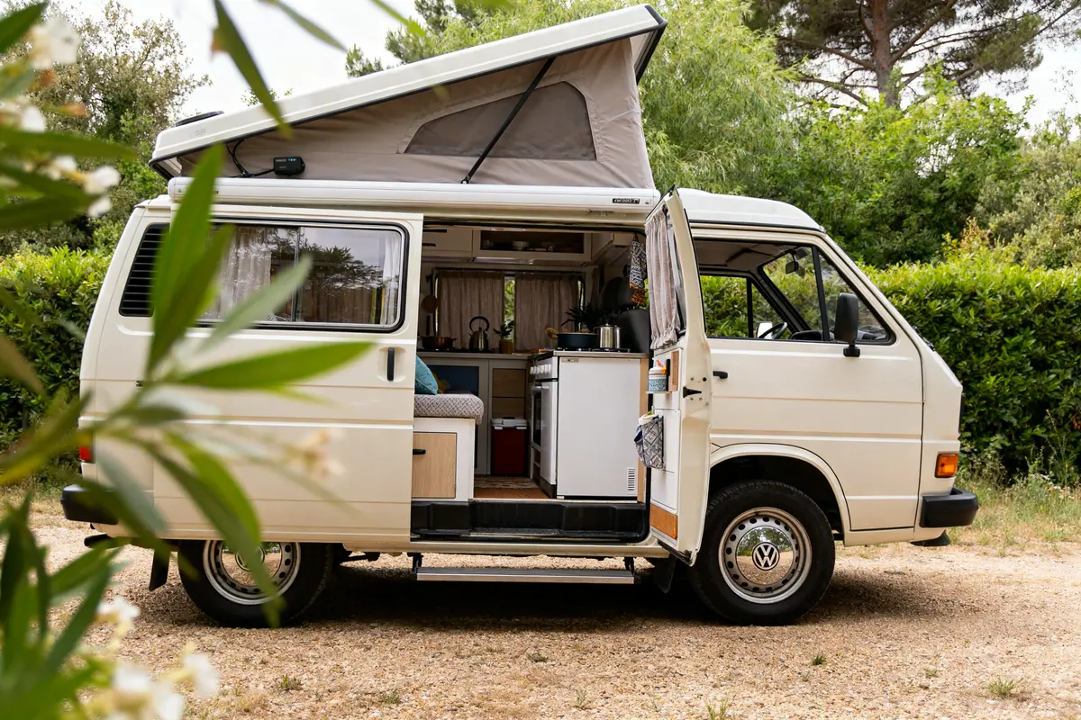 Van aménagé avec toit relevable, intérieur visible, modèle Volkswagen California pop-up.