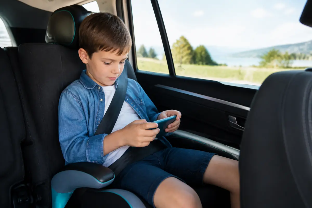 Un garçon ceinture attachée joue sur un smartphone dans une voiture.