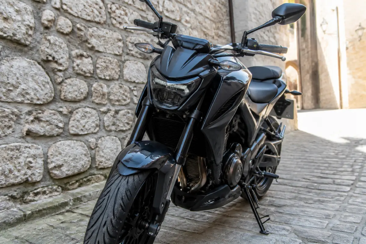 Moto noire garée sur une rue pavée, murs de pierre claire en arrière-plan.